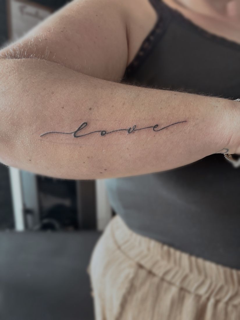 Schriftzug love in einer durchgehenden Linie am Unterarm